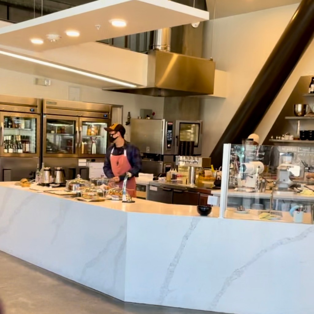 Interior marble counter with a barista behind bar wearing an apron and a mask at Ten by Bar Nine in Marina Del Rey